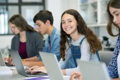 Lächelnde Schülerin in moderner Schulklasse arbeitet am Laptop – digitales Lernen im Unterricht