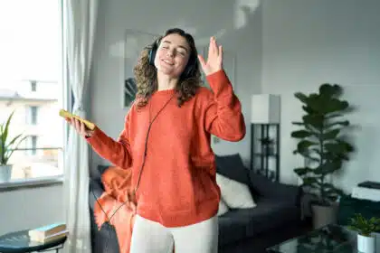 Musik hören mit Kopfhörern – Frau tanzt fröhlich im Home-Outfit im modern eingerichteten Wohnzimmer