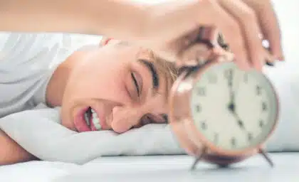 Als Teenager schlaftrunken den Wecker ausschalten – Symbolbild für Aufstehen, Schlafmangel und Morgenroutine