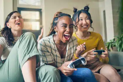 Drei junge Frauen spielen begeistert Videospiele auf der Couch – Gaming, Freundschaft und Spaß im Wohnzimmer