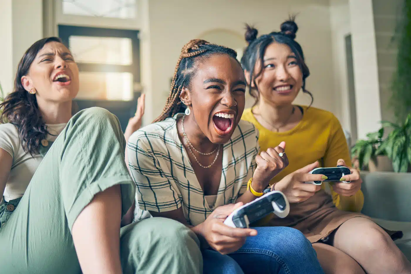 Drei junge Frauen spielen begeistert Videospiele auf der Couch – Gaming, Freundschaft und Spaß im Wohnzimmer