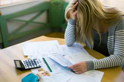 Gestresste Frau mit Mahnungen, Taschenrechner und wenig Kleingeld – Symbolbild für finanzielle Belastung und Steuererklärung