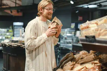 Mann schnuppert genüsslich an einer verpackten Brotscheibe in der Backwarenabteilung eines Supermarkts – Symbolbild für Brotliebhaber oder Einkauf mit allen Sinnen.