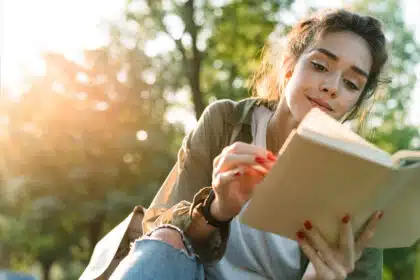 Junge Frau liest entspannt ein Buch im Park bei Sonnenuntergang