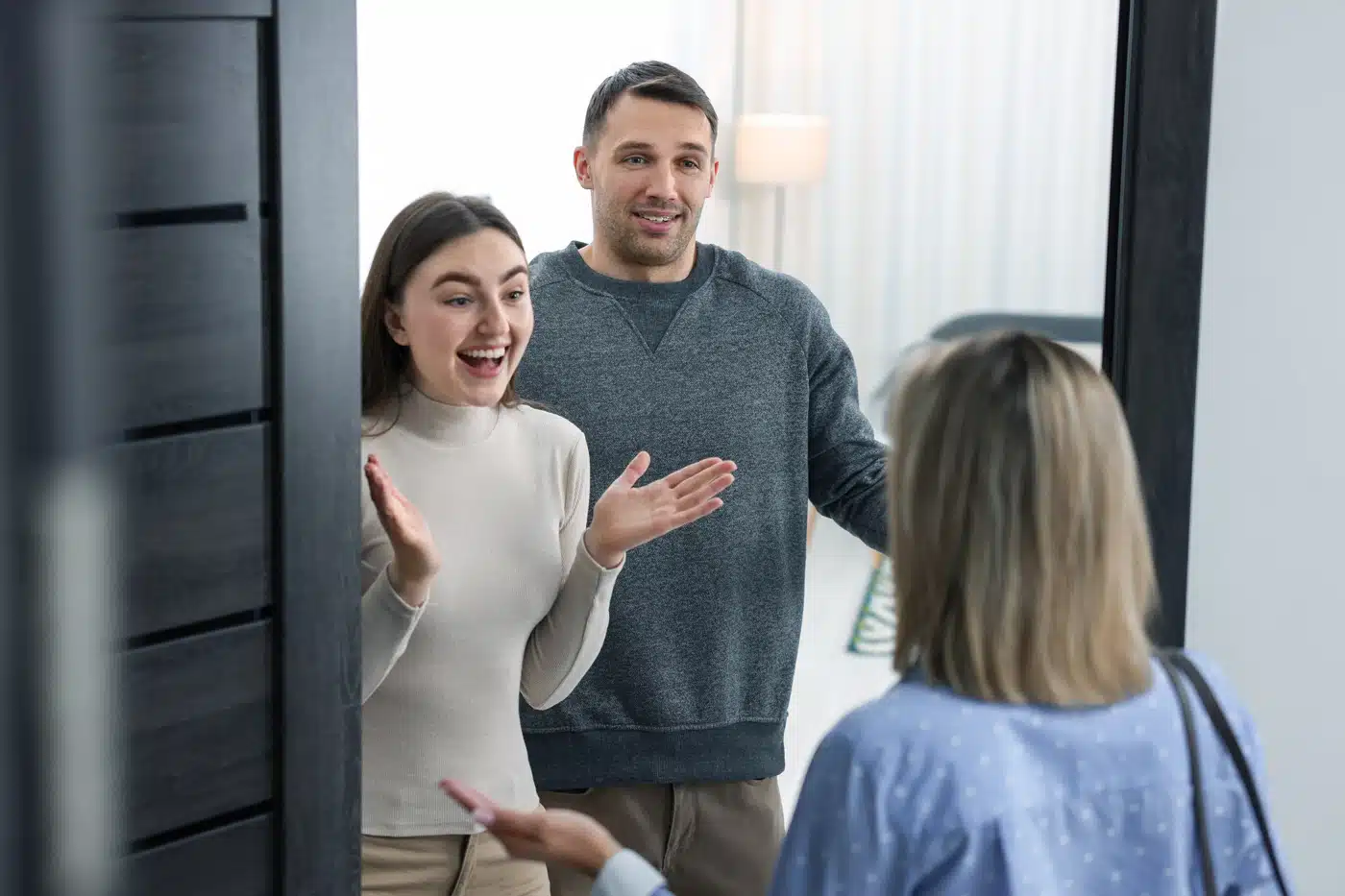 Paar öffnet die Haustür und begrüßt eine Frau freudig