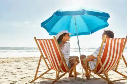 Paar entspannt unter blauem Sonnenschirm in Liegestühlen am Strand – Sonne, Meer und Urlaubsfeeling pur