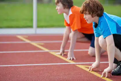 Zwei Jungen in Startposition auf der Laufbahn: Hochkonzentriert und bereit zum Sprint beim Leichtathletik-Wettkampf – Symbol für Ehrgeiz, Fokus und sportlichen Einsatz.