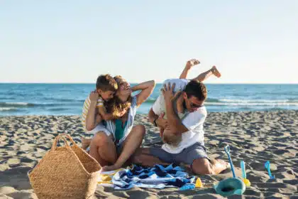 Glückliche Familie spielt am Strand – Eltern toben mit ihren Kindern im Sand vor dem Meer