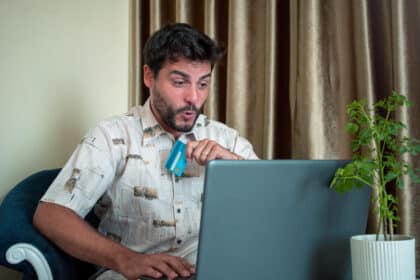 Überraschter Mann beim Online-Shopping auf Verkaufsportalen: Er hält eine Kreditkarte in der Hand und schaut mit erstaunter Miene auf seinen Laptop – symbolisiert Impulskäufe oder überraschende Online-Funde.