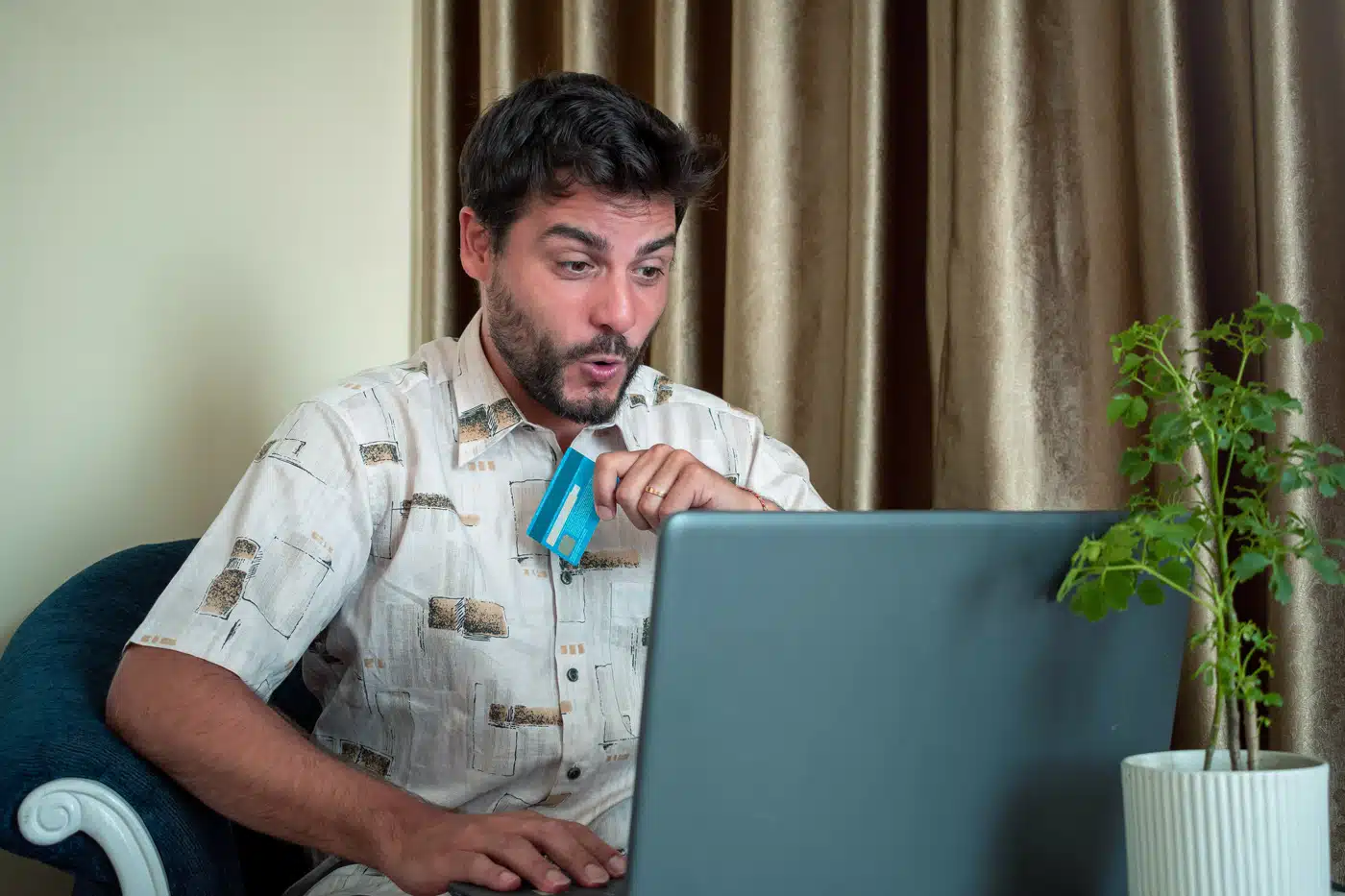 Überraschter Mann beim Online-Shopping auf Verkaufsportalen: Er hält eine Kreditkarte in der Hand und schaut mit erstaunter Miene auf seinen Laptop – symbolisiert Impulskäufe oder überraschende Online-Funde.