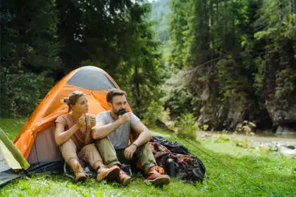 Paar sitzt vor Zelt und trinkt Kaffee beim Camping in der Natur