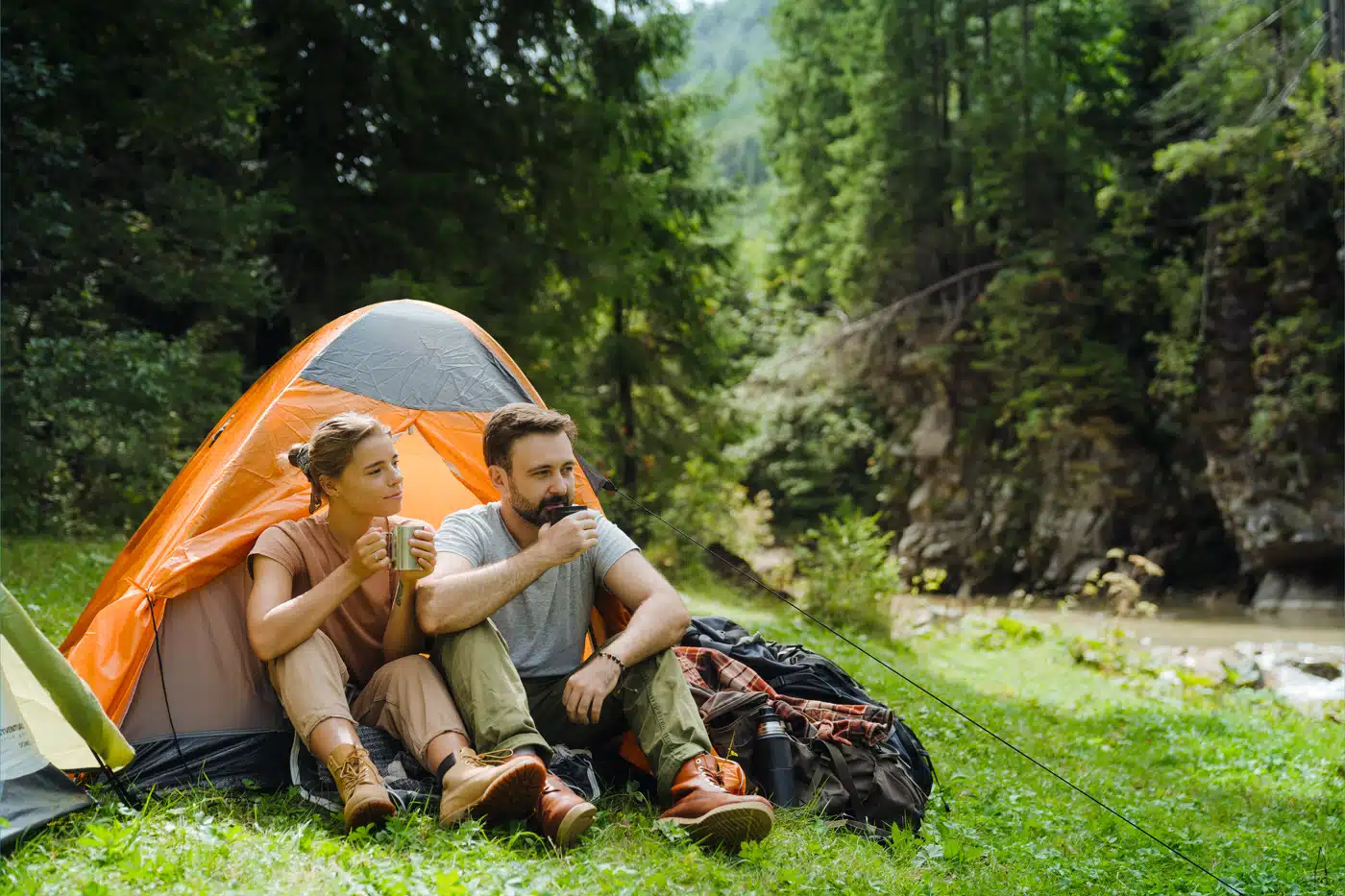 Paar sitzt vor Zelt und trinkt Kaffee beim Camping in der Natur