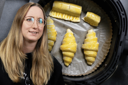 Frau mit skeptischem Blick vor einem Airfryer, in dem ungebackene Teigstücke auf Backpapier liegen – ironischer Küchenmoment zwischen Food-Hack und Fehlversuch.