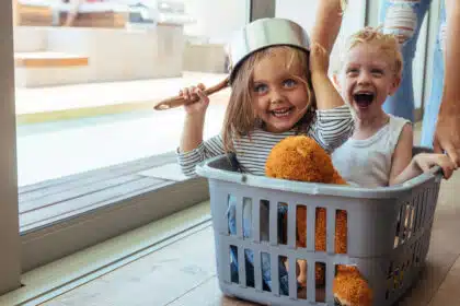 Kinder spielen fantasievoll mit den Eltern und Alltagsgegenständen – Kochtopf als Helm und Wäschekorb als Spielgefährt
