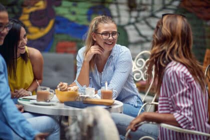 Vier extrovertierte Freunde sitzen lachend im Café, trinken Kaffee und unterhalten sich ausgelassen.
