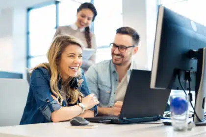 Kollegen im modernen Büro lachen gemeinsam während der Arbeit am Computer.
