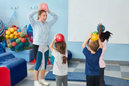 Kinderturnen in der Halle: Trainerin zeigt Bewegung mit Ball.