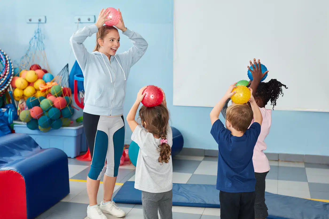 Kinderturnen in der Halle: Trainerin zeigt Bewegung mit Ball.
