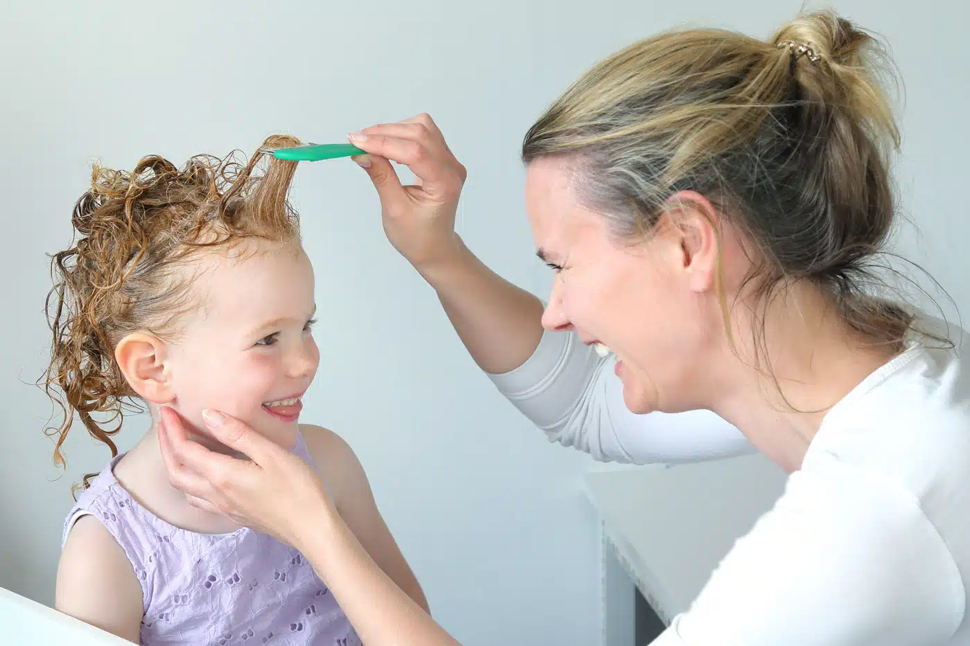 Mutter entfernt mit speziellem Kamm Kopfläuse bei ihrer Tochter – Symbolbild für Läusebefall im Kindergarten oder in der Schule.