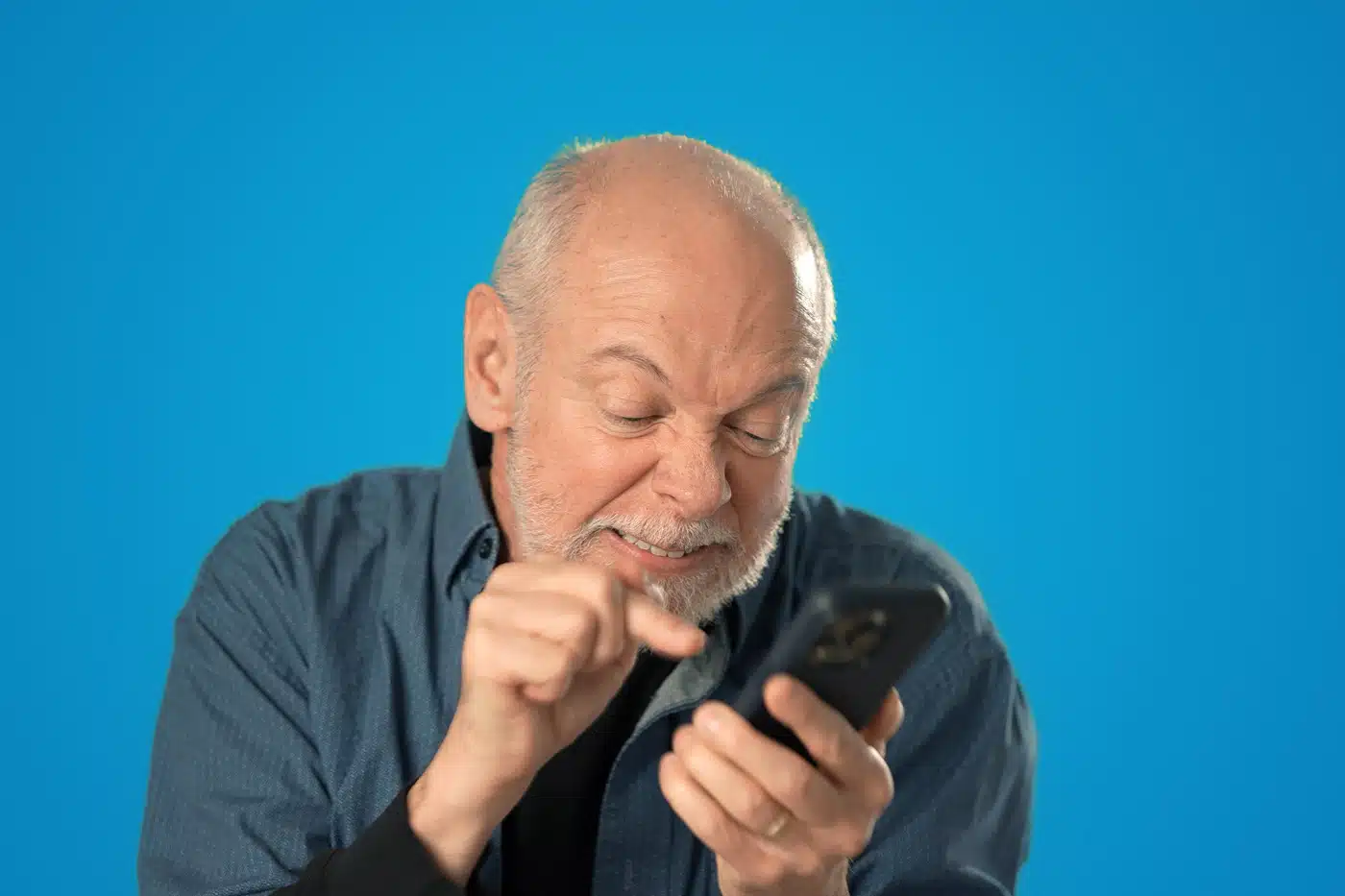 Älterer Mann schaut genervt auf sein Smartphone und tippt frustriert – Symbolbild für Technikprobleme oder digitale Überforderung.