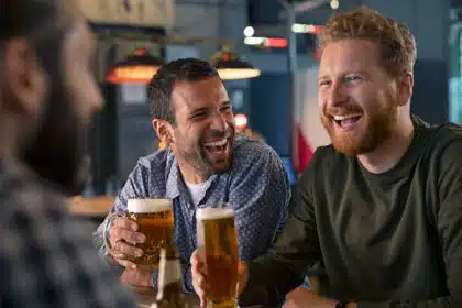 Drei Männer sitzen in einer Bar, trinken Bier und lachen gemeinsam über deutsche Sprüche.