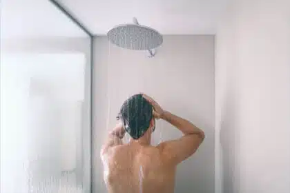 Mann steht unter der Dusche und wäscht sich die Haare mit Shampoo.