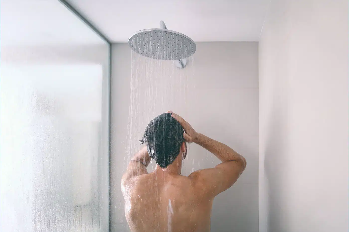 Mann steht unter der Dusche und wäscht sich die Haare mit Shampoo.
