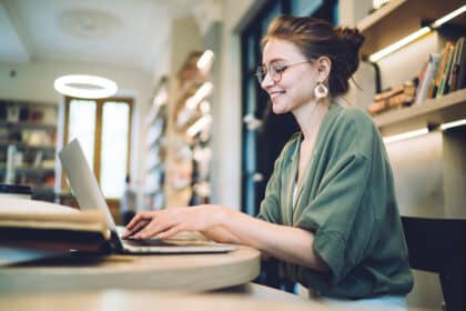 Junge Frau lernt online am Laptop in einer Bibliothek und macht ihr Fernstudium.