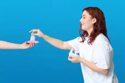 Junge Frau nimmt ein Feuchttuch aus einer kleinen rosa Verpackung, die ihr von einer anderen Hand gereicht wird.