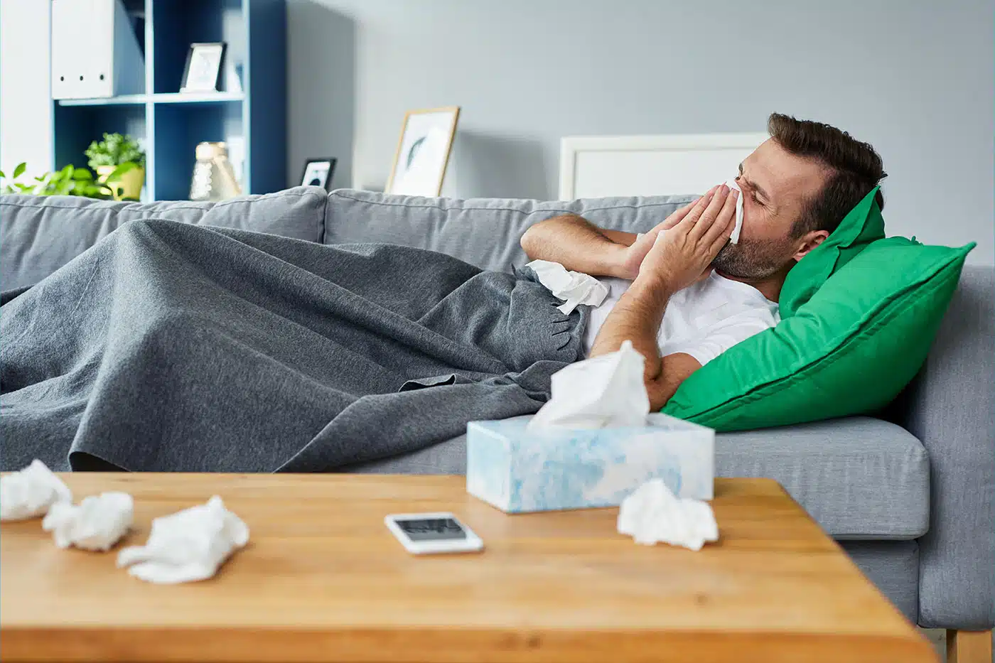 Mann liegt erkältet auf dem Sofa und putzt sich die Nase.