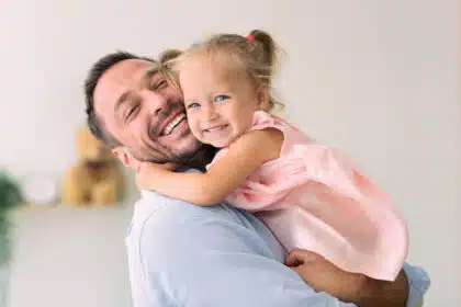 Lächelnder Papa umarmt seine kleine Tochter, beide strahlen vor Freude.