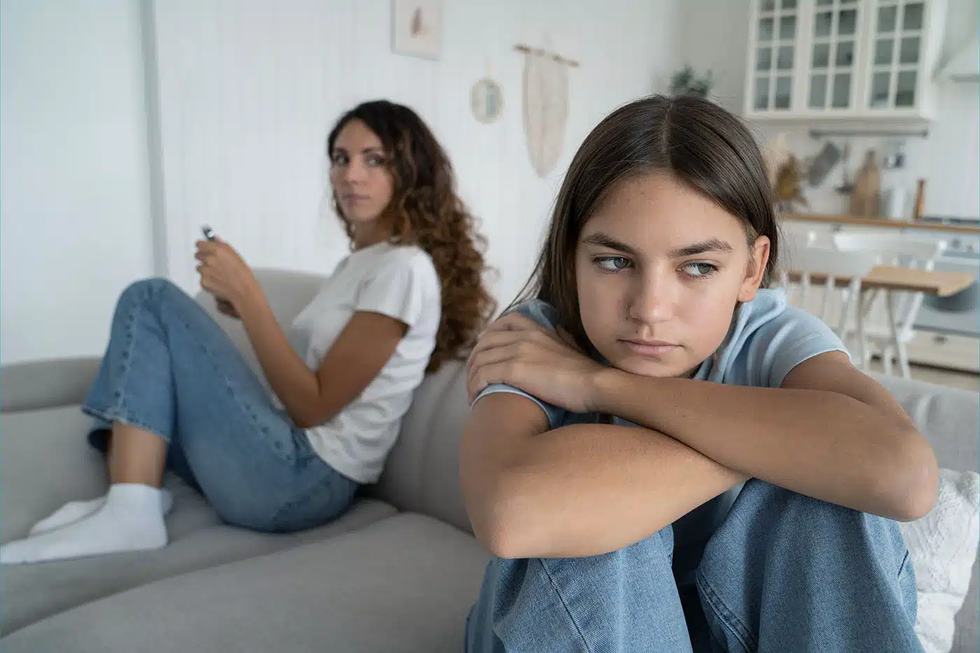 Mutter und Tochter sitzen distanziert auf dem Sofa und haben sich gerade gestritten.