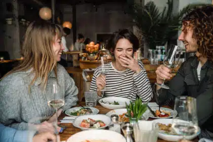 Drei Freunde sitzen im Restaurant am Tisch, lachen und genießen gemeinsam ihr Essen.