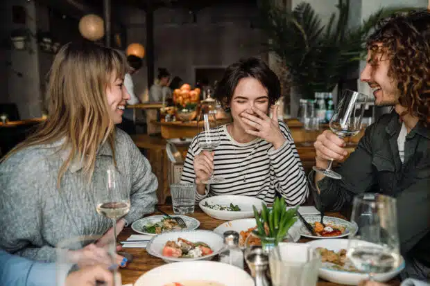 Drei Freunde sitzen im Restaurant am Tisch, lachen und genießen gemeinsam ihr Essen.