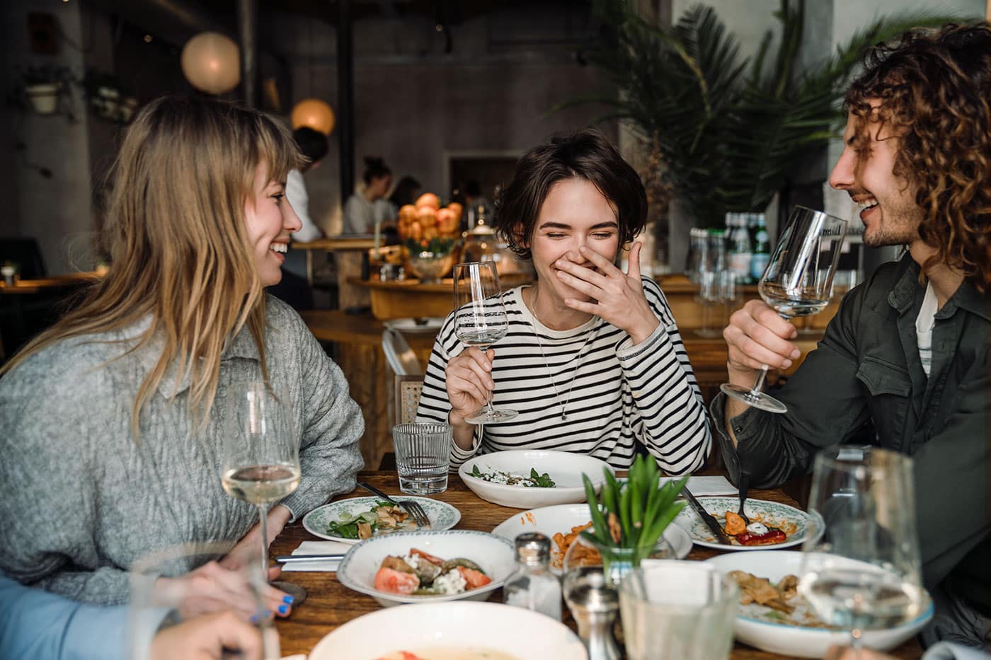 Drei Freunde sitzen im Restaurant am Tisch, lachen und genießen gemeinsam ihr Essen.