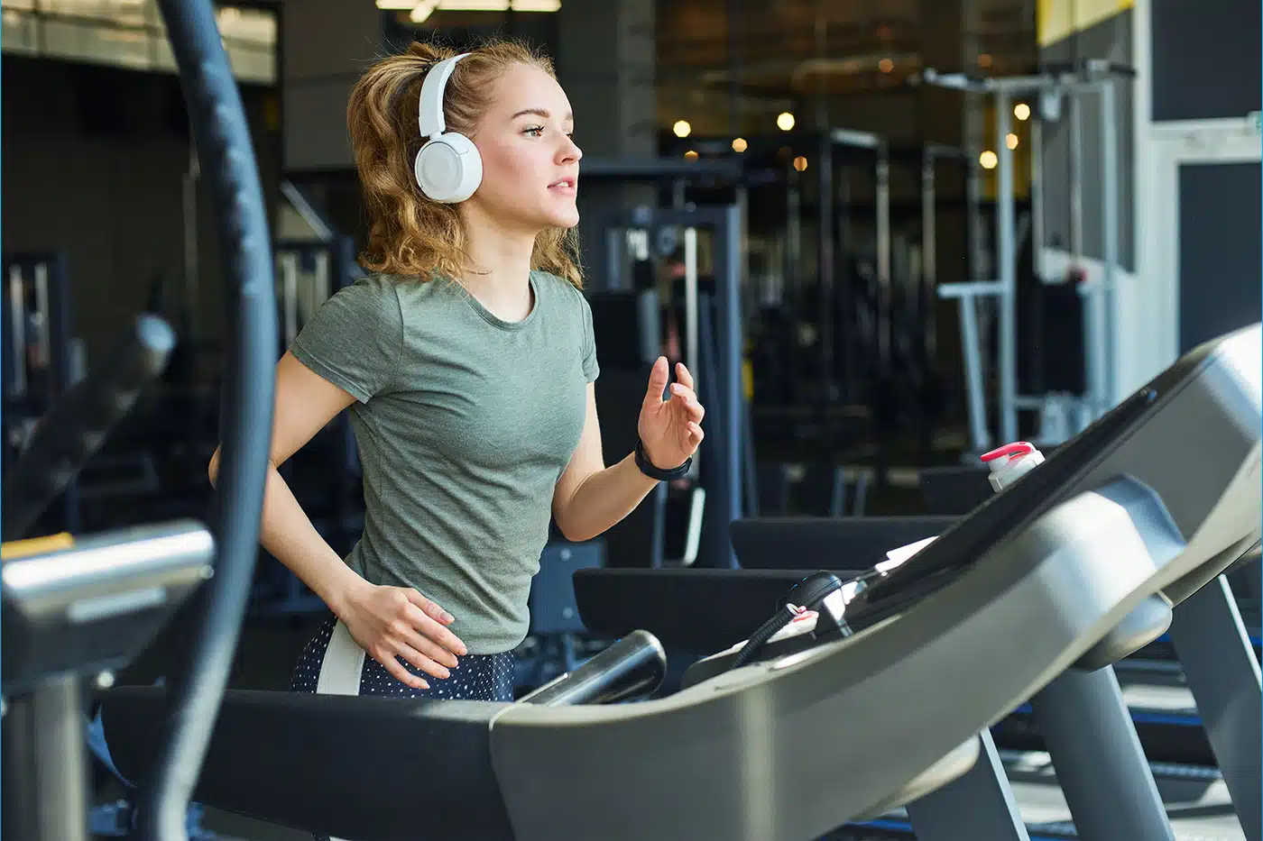 Junge Frau mit Sportklamotten joggt auf dem Laufband im Gym.