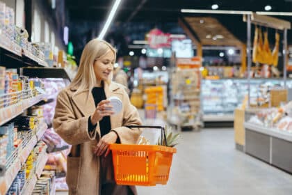 Junge Frau mit Einkaufskorb kauft Lebensmittel im Supermarkt ein.