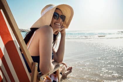 Glückliche Frau im Liegestuhl sieht erholt aus und genießt den Sommerurlaub am Strand.