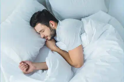 Mann liegt zugedeckt im Bett und schläft.