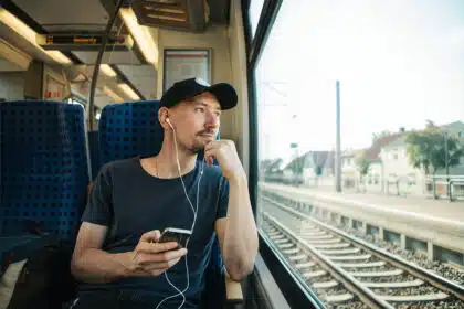 Junger Mann mit Kopfhörern im Ohr schaut aus dem Fenster während er Bahn fährt.