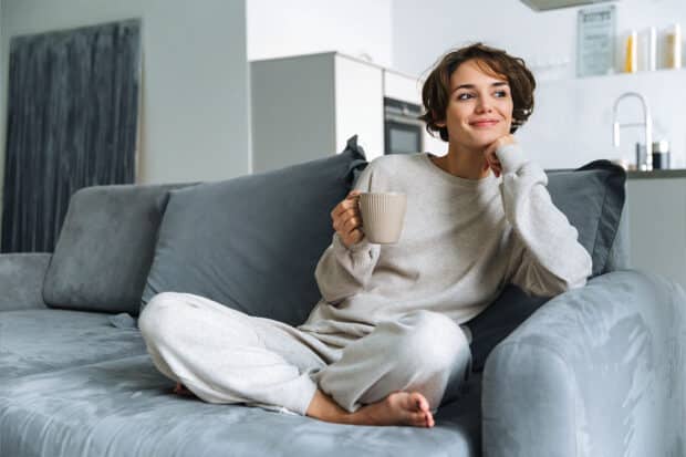 Frau sitzt auf der Couch mit einer Tasse in der Hand und macht es sich gemütlich.