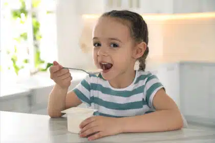 Junges Mädchen sitzt in der Küche und isst glücklich ihren Joghurt.