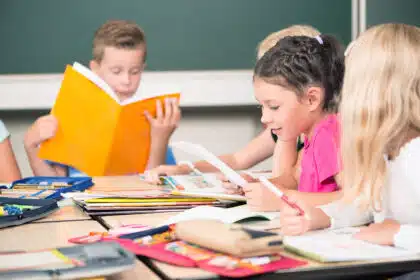 Kinder sitzen in der Schule am Tisch und beschäftigen sich mit ihren Schulmaterialien.