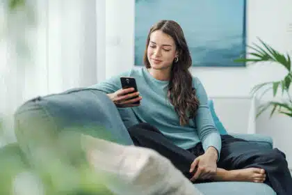 Mädchen im Teenager Alter sitzt daheim auf dem Sofa und ist am Handy.
