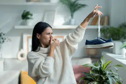 Eine Frau hält geekelt ein paar Schuhe hoch und hält sich die Nase zu.
