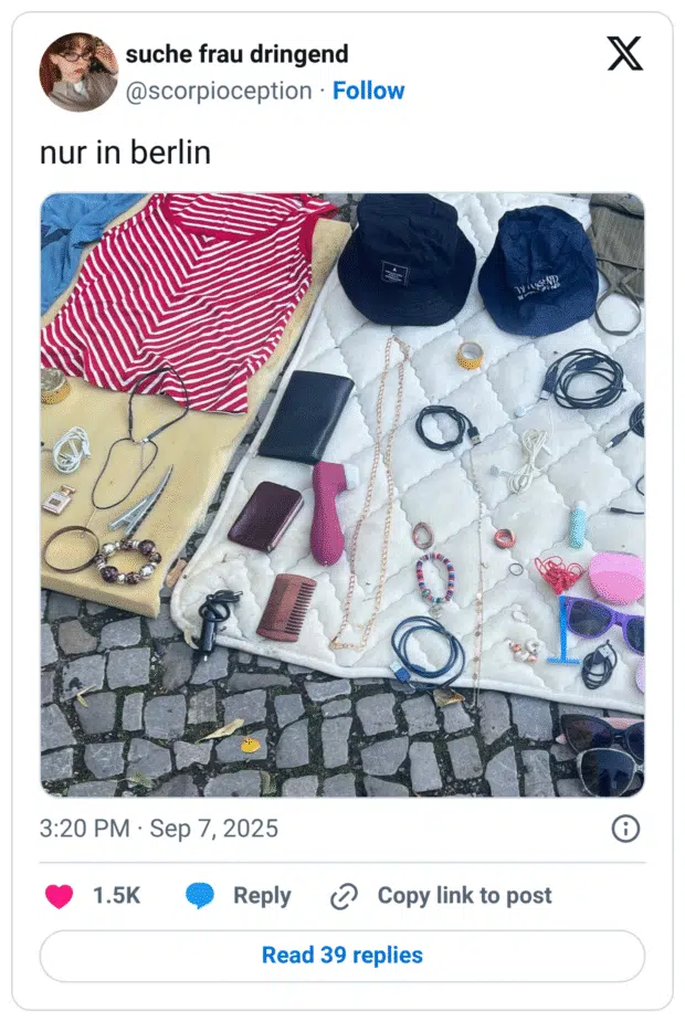 Straßenflohmarkt-Szene auf Kopfsteinpflaster: Auf zwei Decken liegen wild gemischt Secondhand-Kleinteile – ein rot-weiß gestreiftes Top, zwei schwarze Bucket-Hats, lange Ketten, Armbänder, Haarklammern, Kamm, pinkes Gesichtsreinigungsgerät, Rasierer, Sonnenbrillen, Portemonnaies, eine Rolle Klebeband sowie viele Lade- und Audiokabel und In-Ear-Kopfhörer.