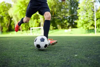 Fußballspieler kickt Fußball auf Fußballplatz.