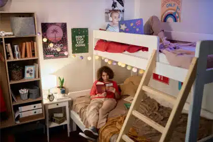 Zwei Jugendliche verbringen den Abend in einem gemütlichen Hochbett: Eines liest auf der unteren Etage ein Buch, während das andere auf der oberen Etage mit Kopfhörern auf einem Tablet schaut.