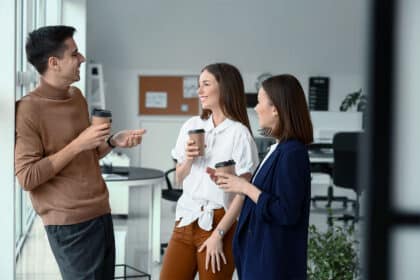 Drei lächelnde Kollegen unterhalten sich bei einer Kaffeepause in einem modernen Büro.