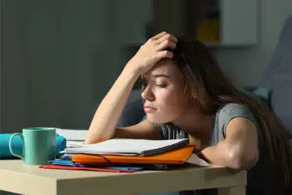 Eine Schülerin sitzt mit traurigem und erschöpftem Blick an ihrem Schreibtisch vor Schulbüchern.